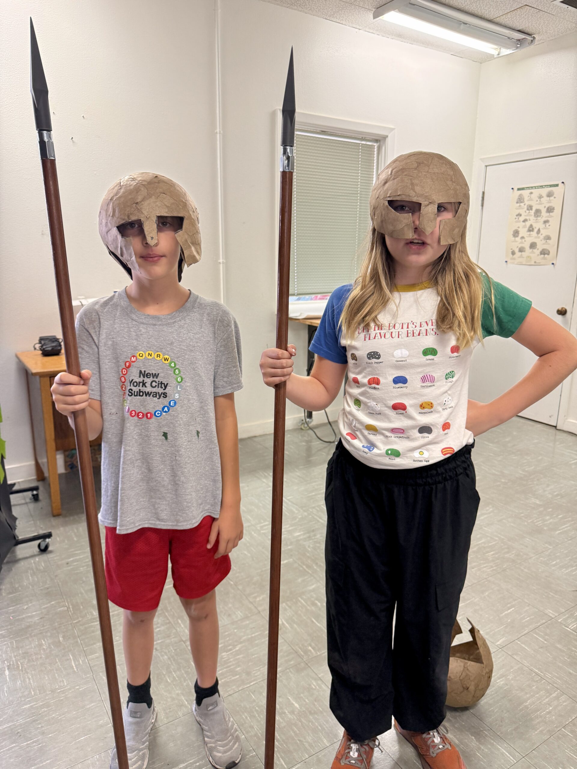 Two First Pres students wearing handmade historical helmets and holding props